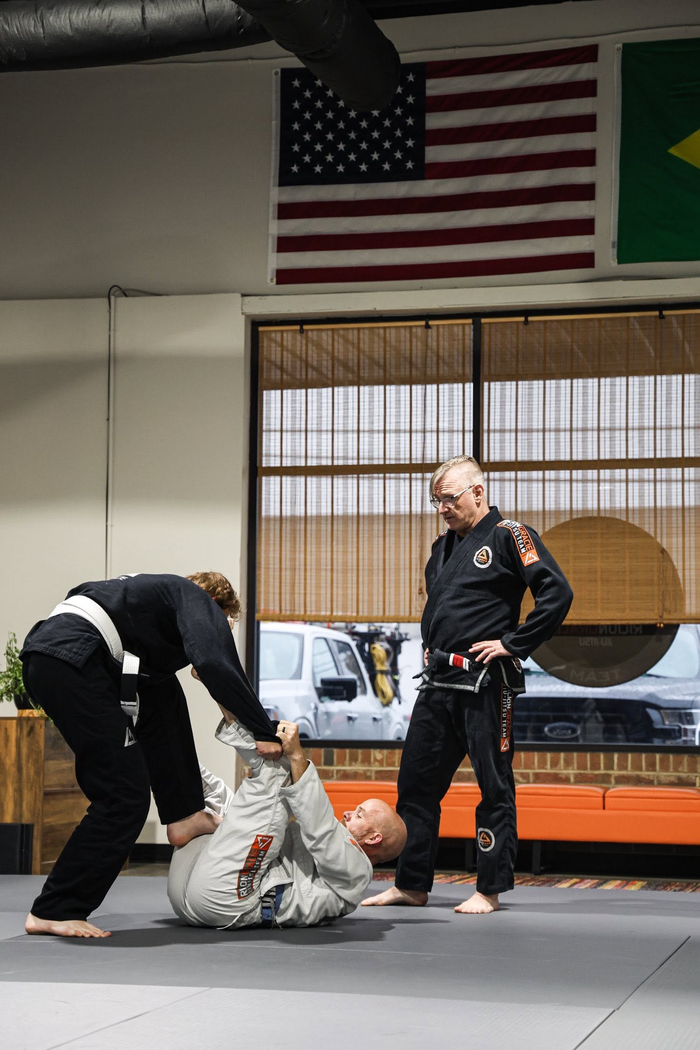 An instructor observing two students practicing a technique on the mat