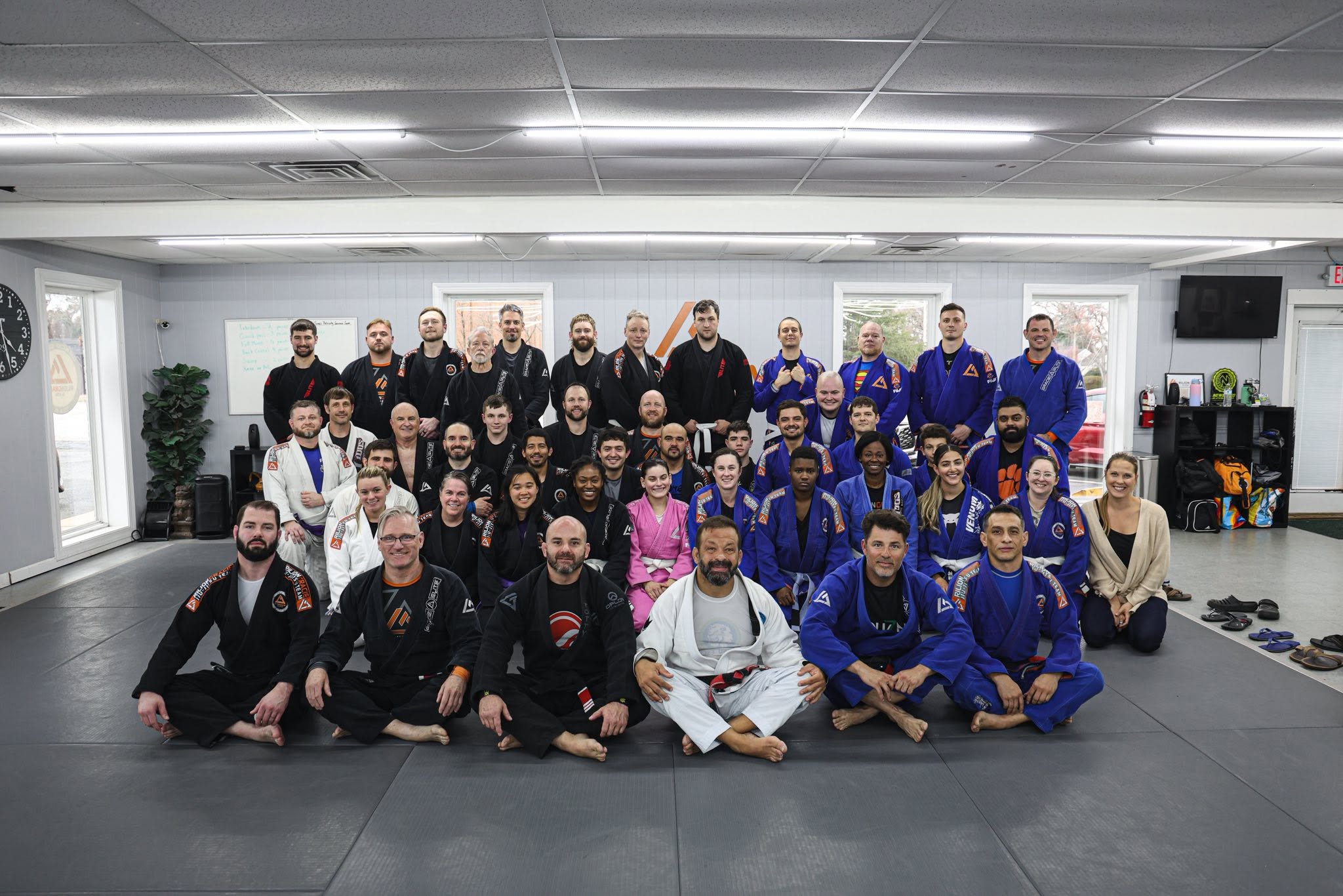 A large group of jiu-jitsu students and instructors gathered together on the academy mats