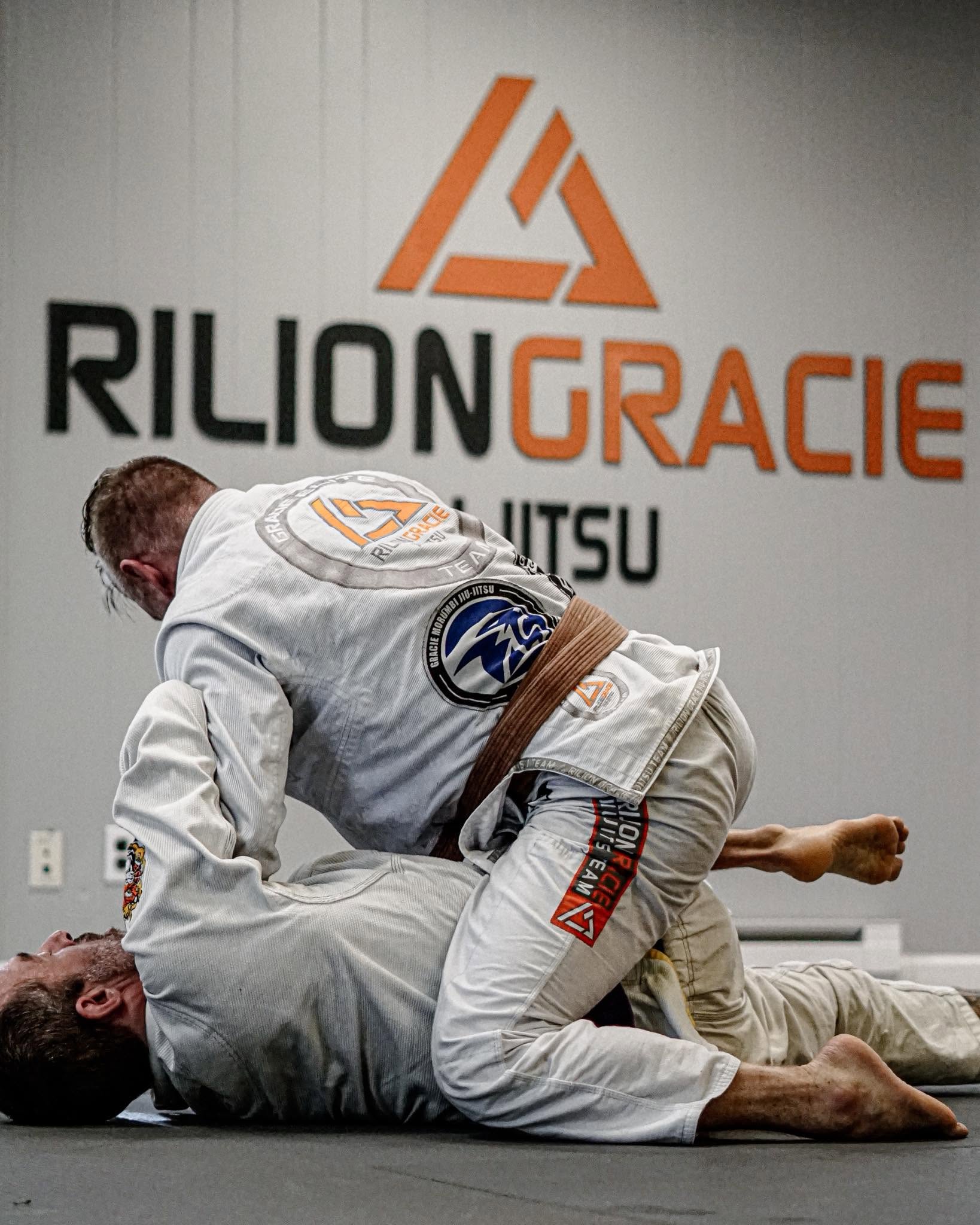 Two jiu-jitsu practitioners training in front of the Rilion Gracie academy wall